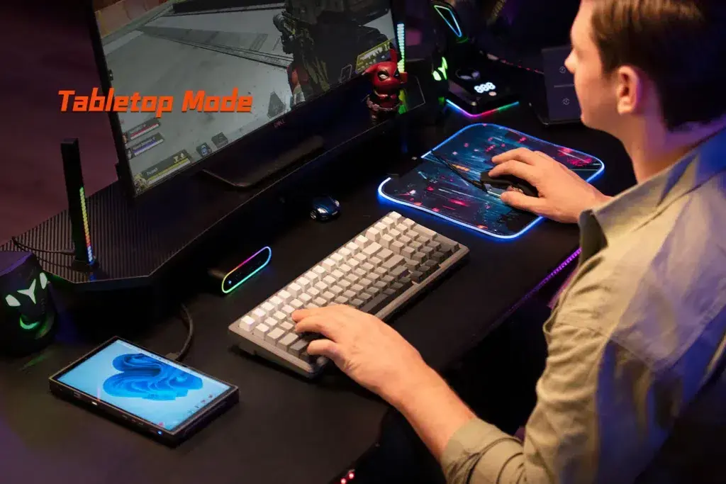 A user playing a first-person shooter on an external monitor connected to the ONEXPLAYER X1 Mini, showcasing its Tabletop Mode functionality for desktop-like gaming with a keyboard and mouse.