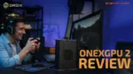 Smiling gamer using a controller while playing a racing game on a desktop setup connected to the ONEXGPU 2 eGPU, with DroiX and OneXPlayer logos and the text 'ONEXGPU 2 REVIEW' prominently displayed.