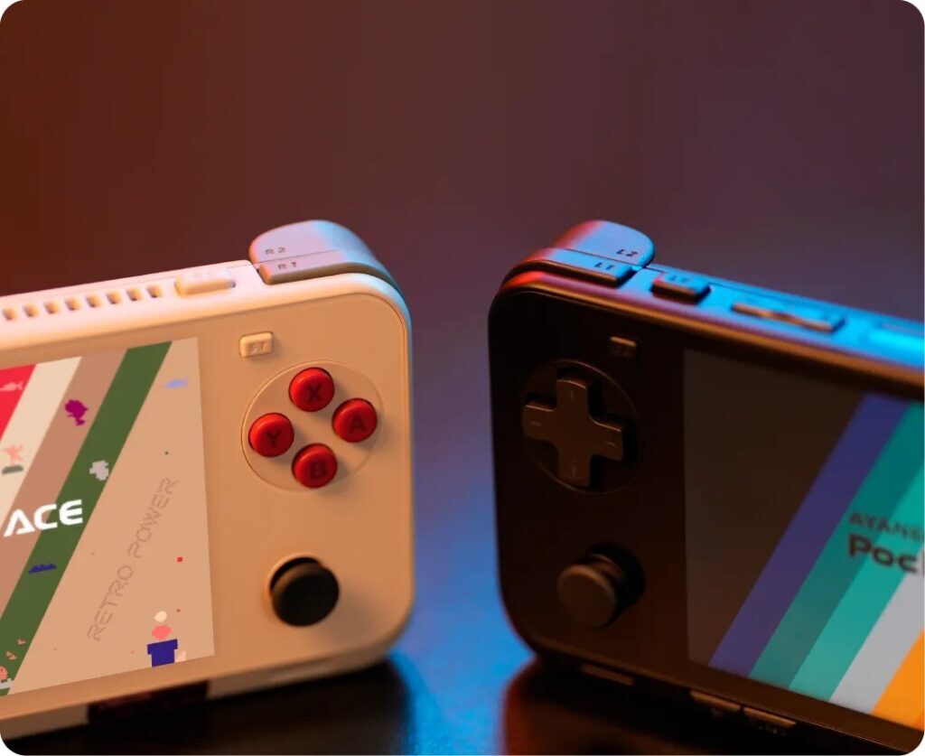 Two AYANEO Pocket ACE handheld gaming consoles side by side—one white with red buttons labeled 'Retro Power', and one black with dark controls. Both display colorful striped screen graphics, showcasing different color schemes. Lit with warm and cool tones to highlight the hardware design and shoulder buttons.