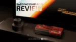 A product review image features a dark red rectangular device, possibly a graphics card or mini PC, with "RX 7600M XT" and "AYANEO GRAPHICS STARS" visible on it. In the background, a screen displays "SPACESHIP AG01 REVIEW" with a logo, and below the device, text reads "AVALIABLE AT DROIX." A small, dark, cylindrical object is to the left of the device.