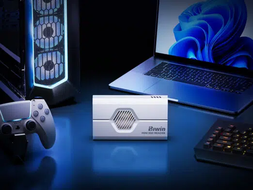 A lifestyle shot of the white SSD reader placed centrally on a blue-lit desk setup, flanked by a gaming PC tower, a game controller, and a laptop.