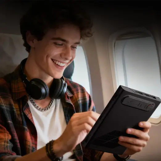 Smiling traveler on airplane holds black ONEXPLAYER 3 handheld gaming PC, angled rear view with textured vents