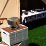 RockTek PJ500 Ultra 1080p smart projector in matte gray, angled on a white crate at a sunny campsite